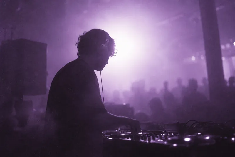 A DJ in profile against a soft violet stage light flare.